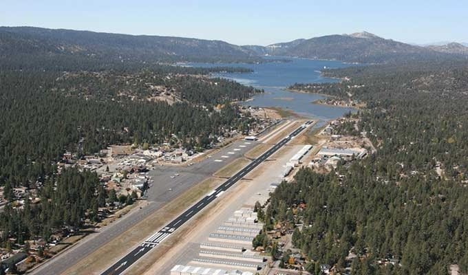 Aerial view of a runway surrounded by forested landscape and a lake in the background.