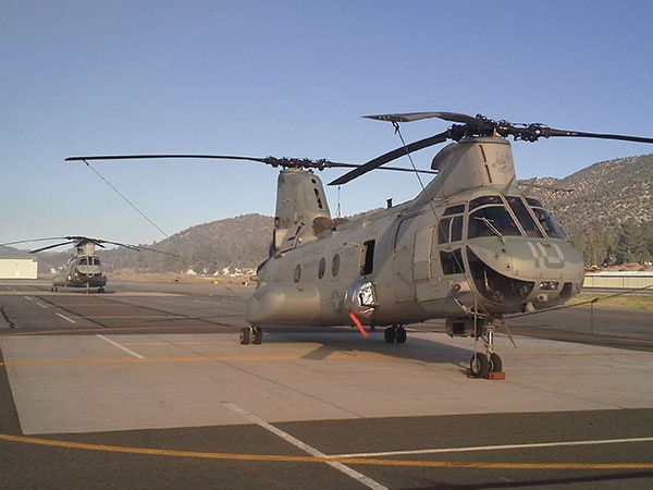 A military helicopter parked on an airstrip, with mountains in the background.