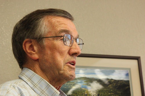 A man wearing glasses and a checkered shirt, with a framed landscape photo on the wall behind him.