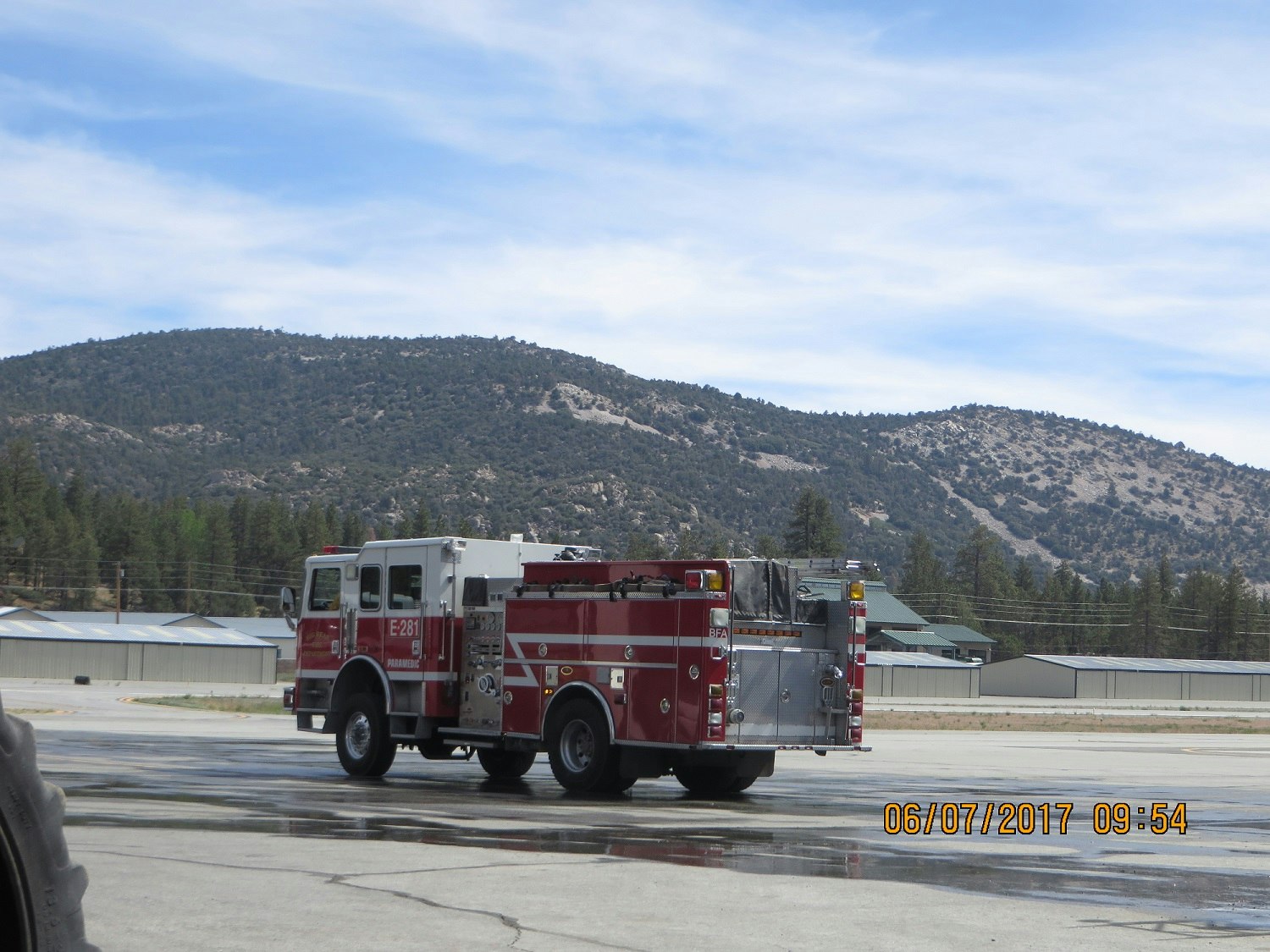 A fire truck driving on a tarmac with mountains and trees in the background.