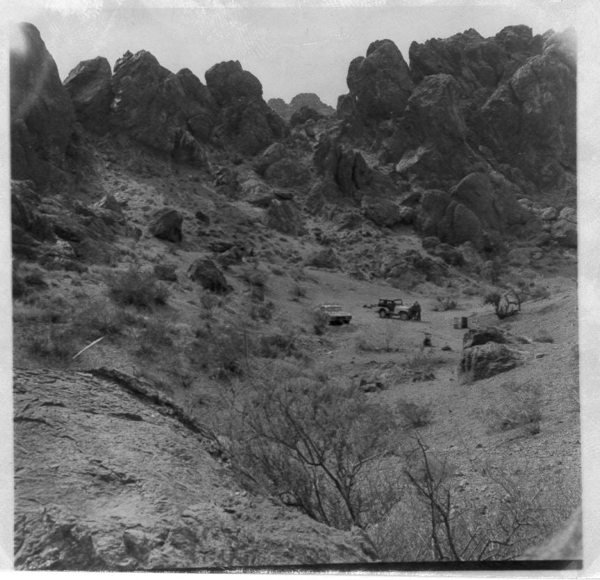 Rocky desert landscape with two vehicles and scattered rocks.