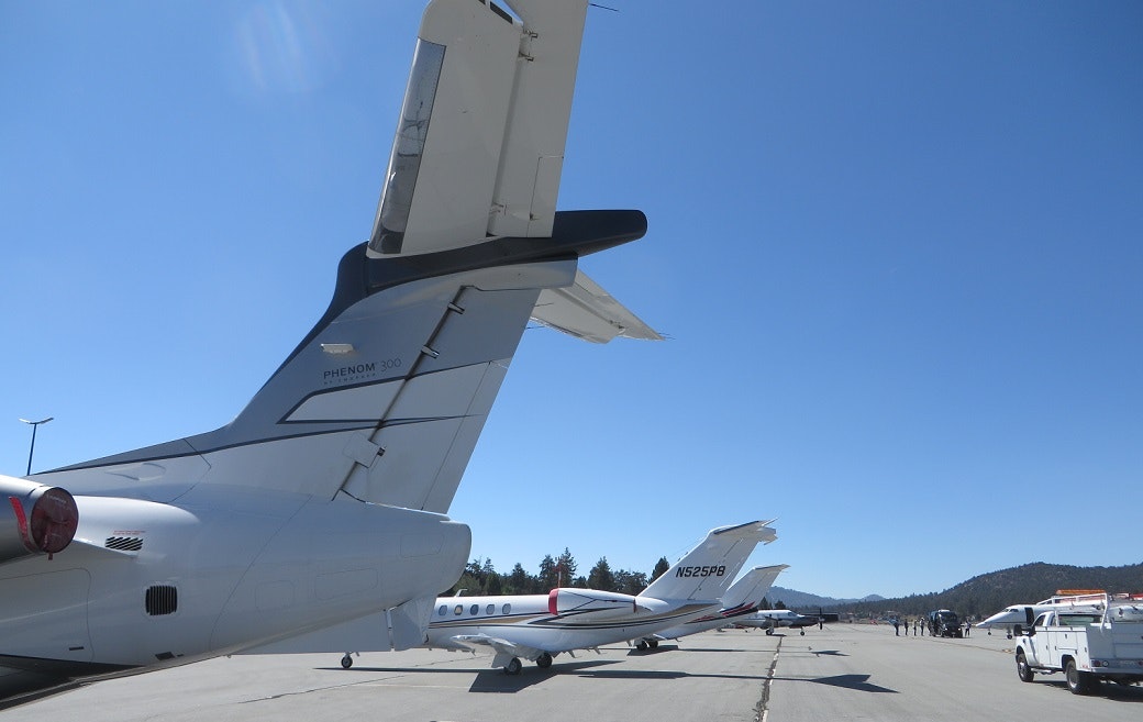 Several private jets parked on an airport tarmac under a clear blue sky.
