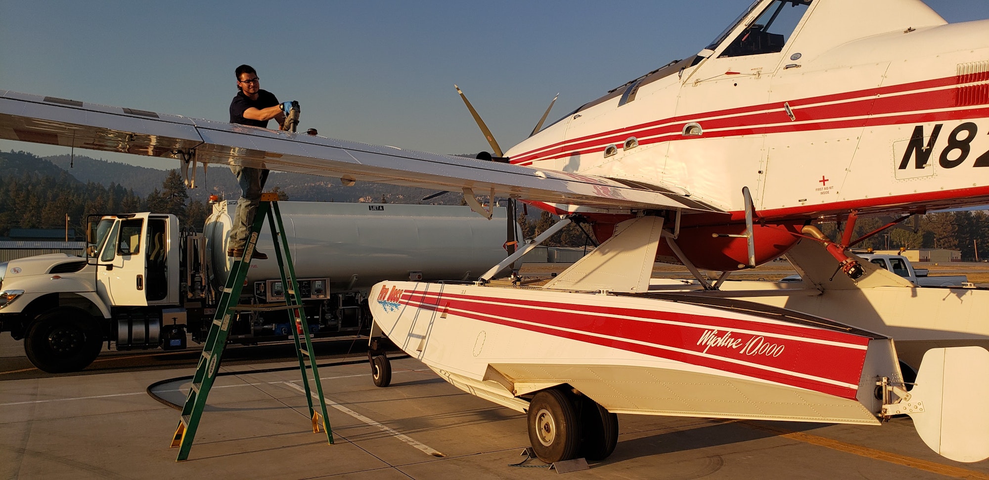 A person on a ladder refuels a plane with a truck in the background.