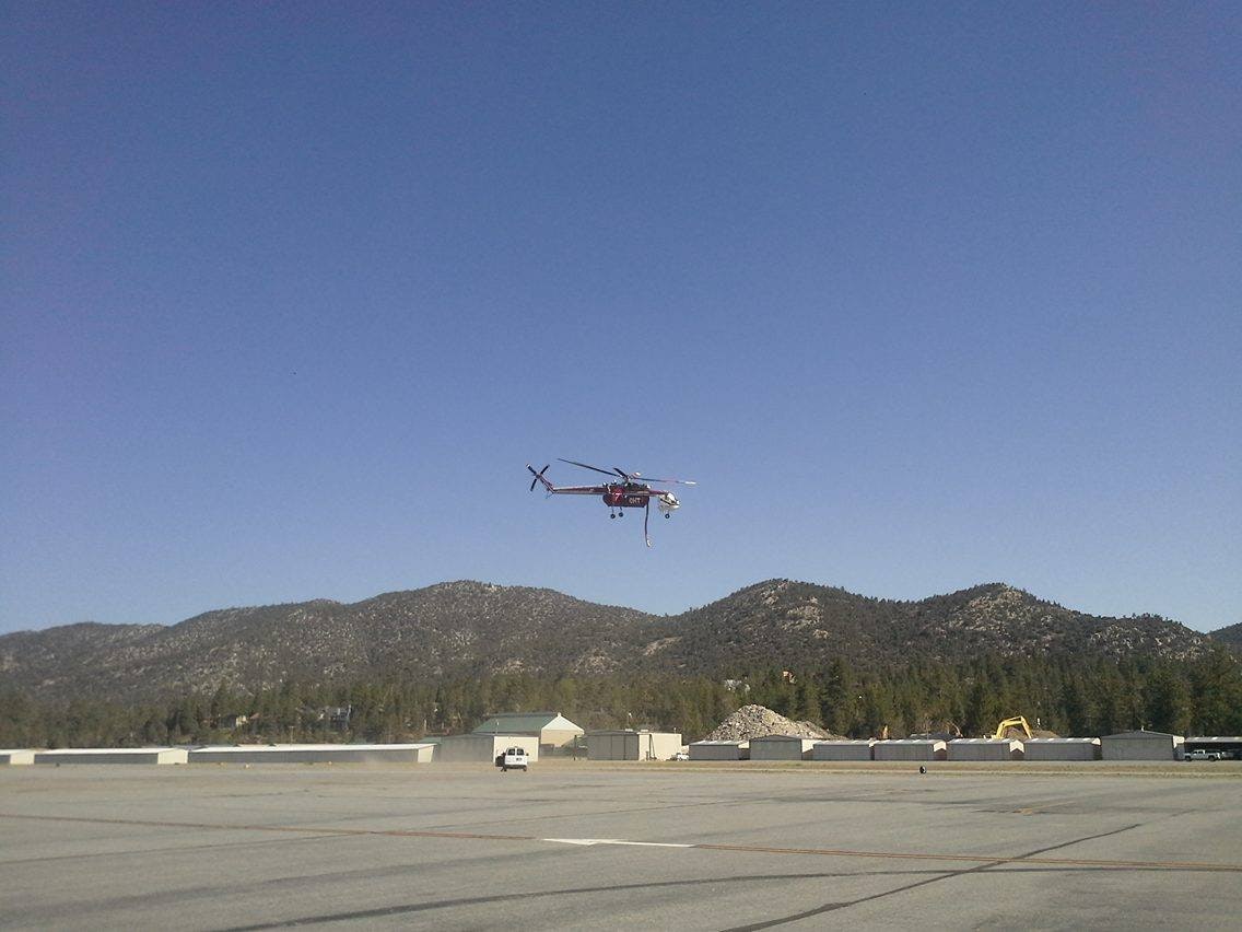 Helicopter hovering over an industrial area with mountains in the background.