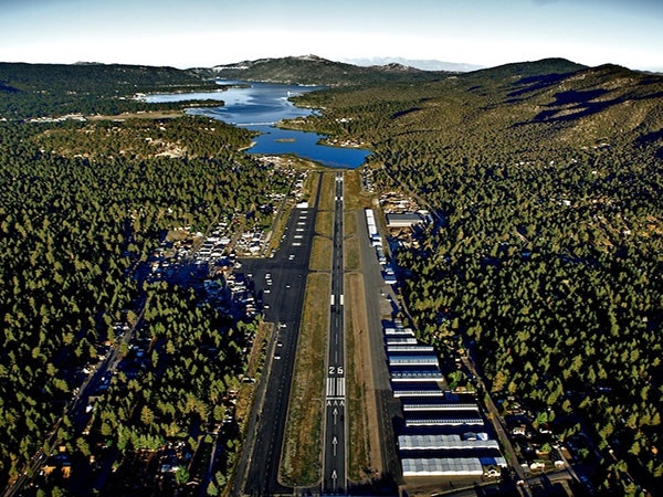 Aerial view of a long runway leading towards a lake, surrounded by dense forests and mountains.