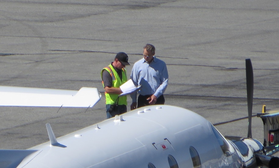 Two people standing by an airplane, discussing documents on an airport tarmac.