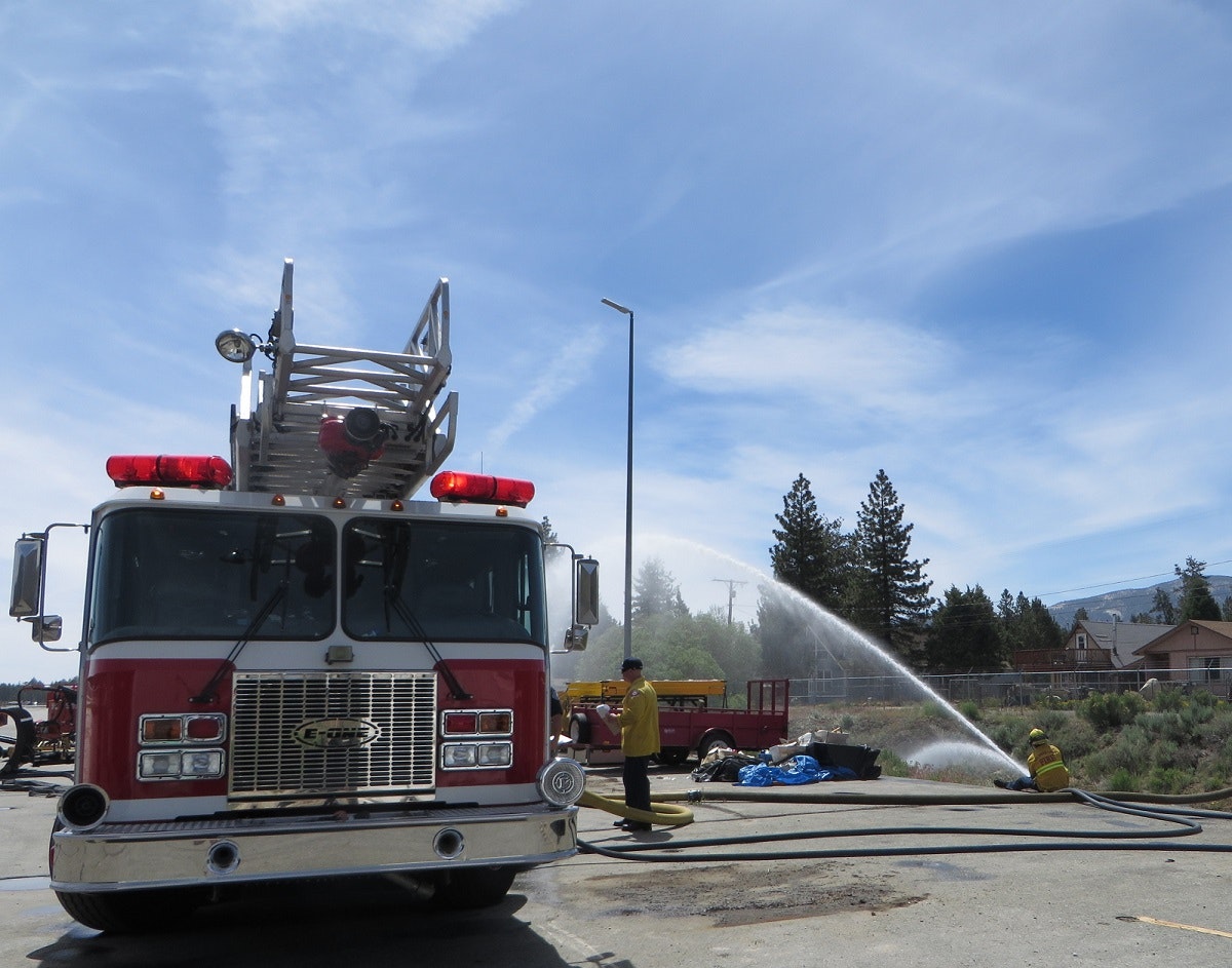 A fire truck and firefighters spraying water from a hose outdoors.