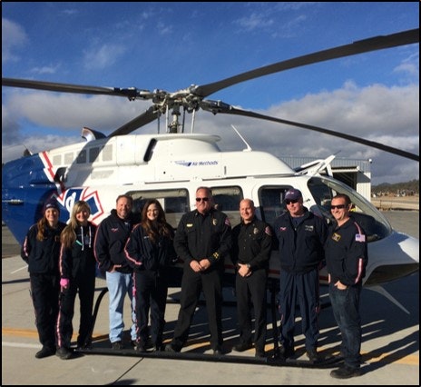 A group of people standing in front of a medical helicopter on a sunny day.