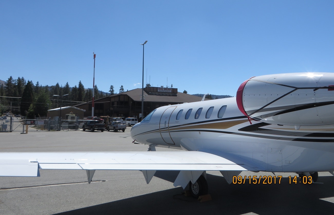 A jet on the tarmac at Big Bear Airport with trees and buildings in the background.