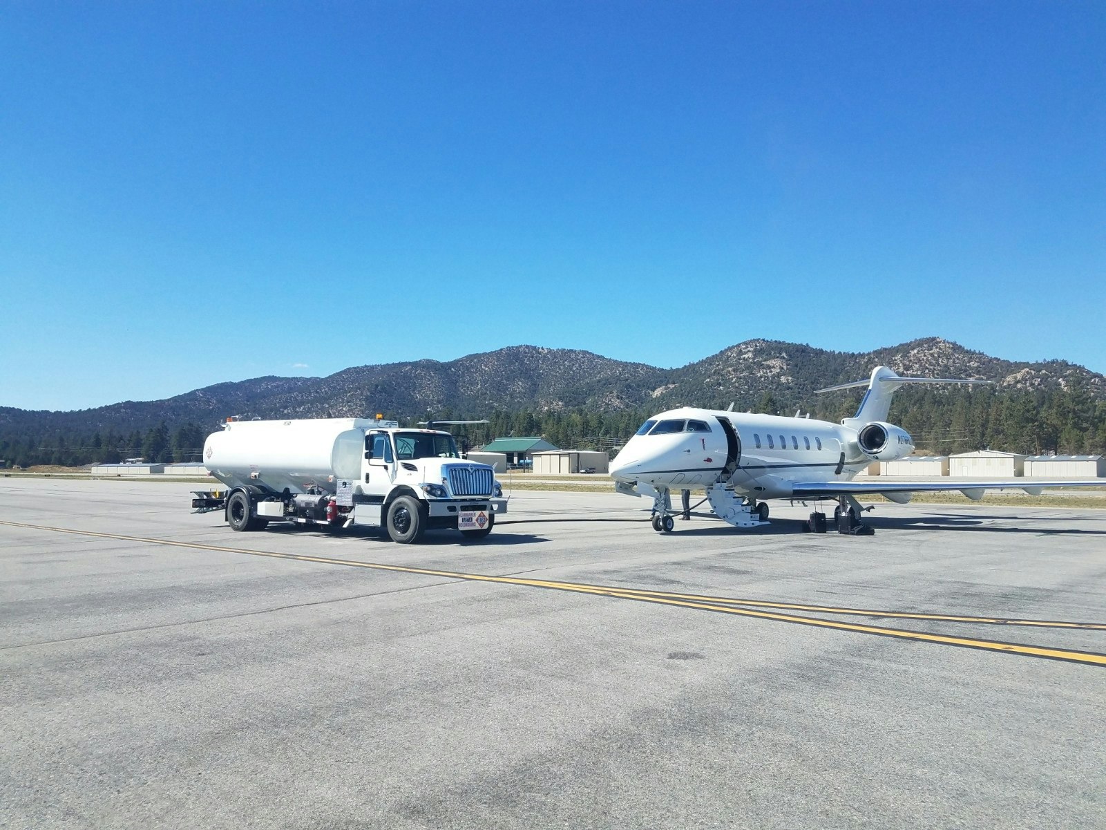 A fuel truck and a private jet on an airport tarmac with mountains in the background.