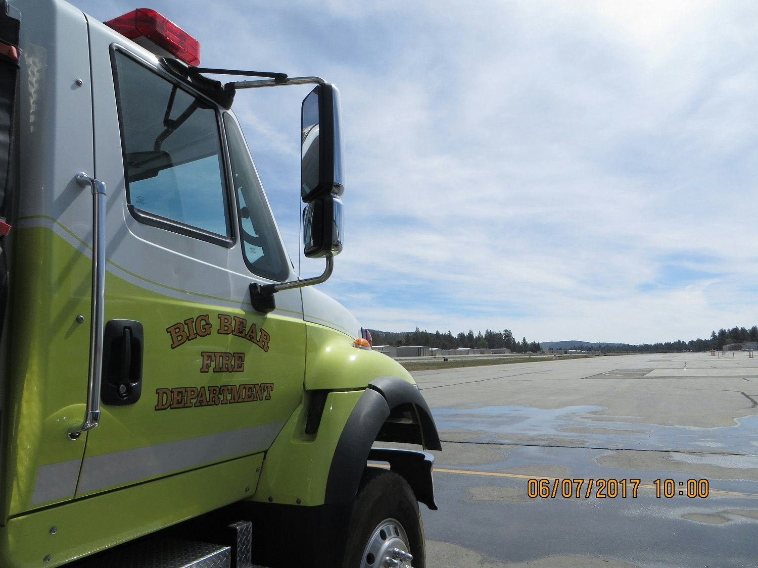 Fire truck labeled "BIG BEAR FIRE DEPARTMENT" parked by an airstrip, under a partly cloudy sky.