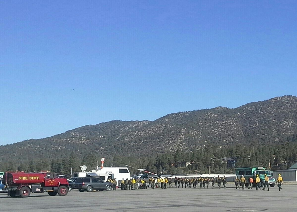 Fire department vehicles and personnel on an airstrip, with mountains in the background.