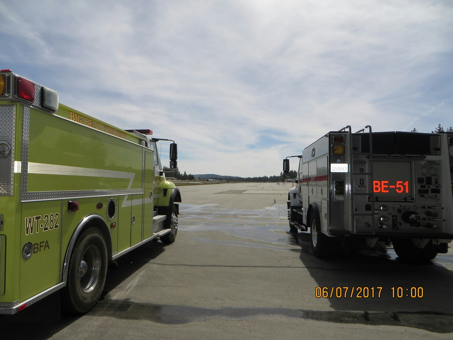 Two fire trucks parked on a paved area under a cloudy sky.