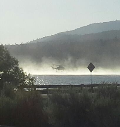 A helicopter over a misty body of water with hills in the background.