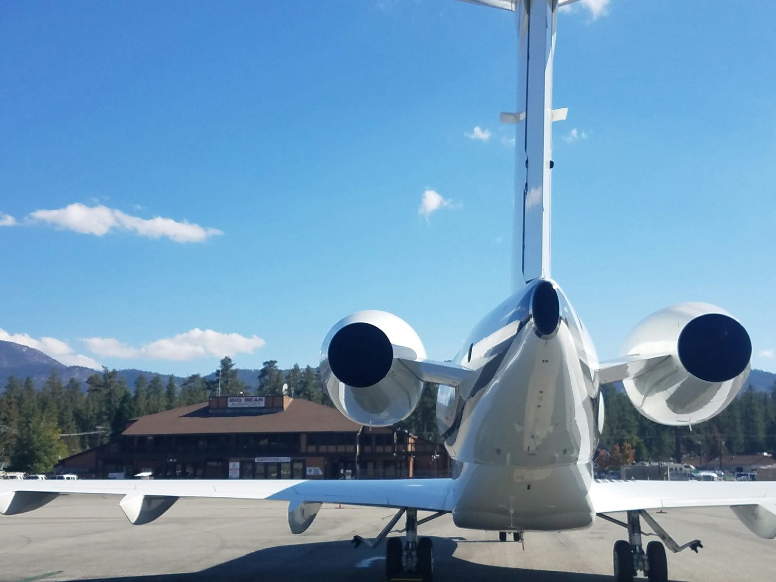A private jet parked on an airport tarmac with a building and trees in the background under a clear blue sky.