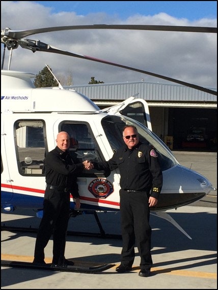 Two people in uniform shaking hands in front of a helicopter on a tarmac.