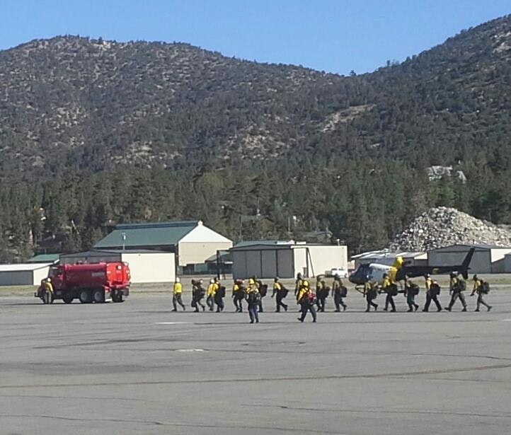 A group of people in yellow uniforms walking on a runway near a red truck, with mountains in the background.
