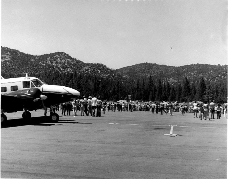 A parked airplane with a crowd of people gathering in front of a scenic mountain backdrop.