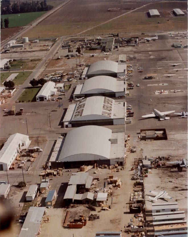 Aerial view of an airport showing hangars, parked airplanes, and nearby buildings.