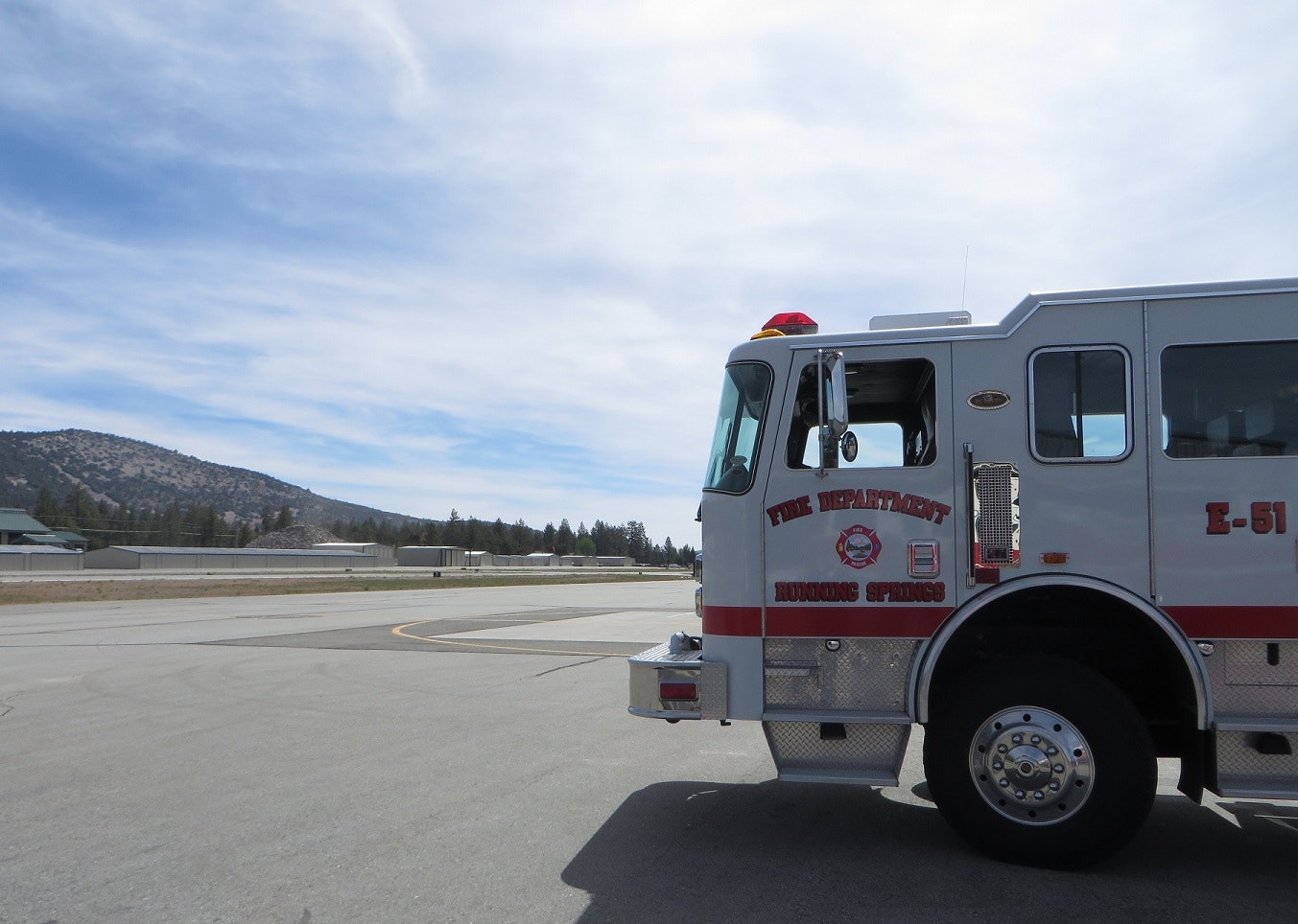 Fire truck from Running Springs Fire Department parked on a road with mountains and an airstrip in the background.
