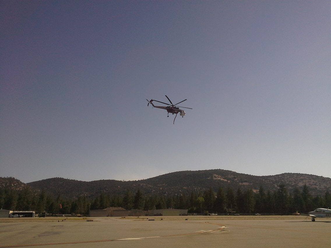Helicopter flying over an airfield with hills and trees in the background.