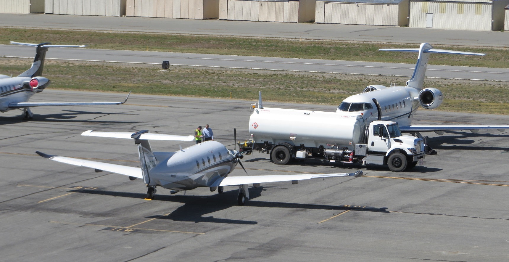 Two airplanes on a tarmac, one being refueled by a truck, with personnel nearby.
