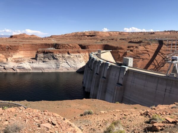 A concrete dam with water reservoir, surrounded by rocky terrain under a clear sky.