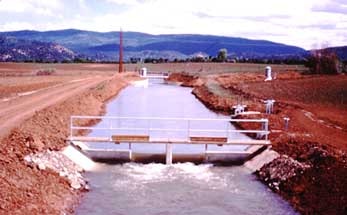 A concrete irrigation channel with a metal control gate, surrounded by a rural landscape.
