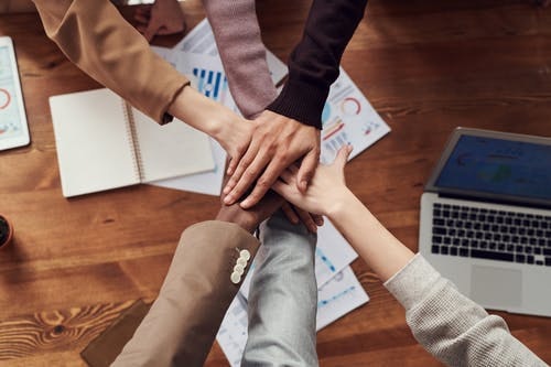 Team stacking hands over a table with business charts and a laptop, signifying unity or teamwork.