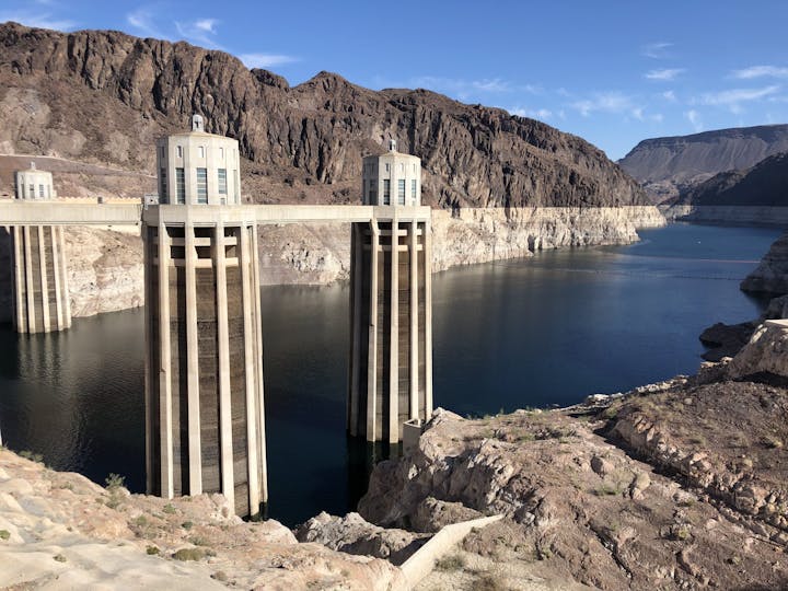 A dam's intake towers, water reservoir, and surrounding rocky terrain under a clear sky.