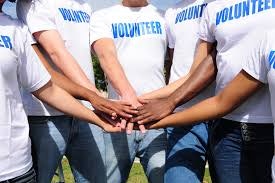 Group of volunteers with hands stacked in unity, all wearing white "VOLUNTEER" t-shirts.