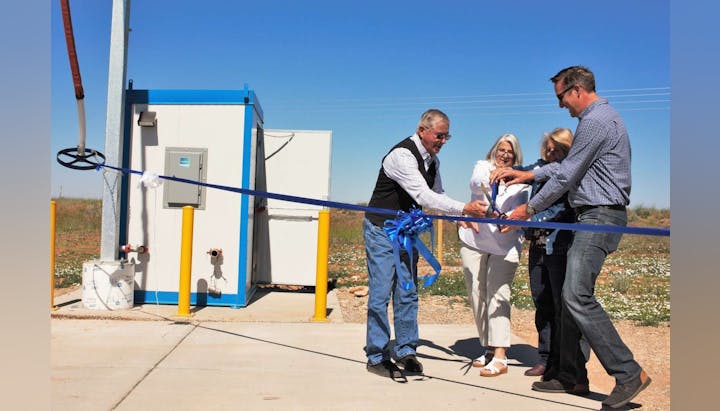 Four people are cutting a blue ribbon at an outdoor event, likely a ceremony or opening of a facility.