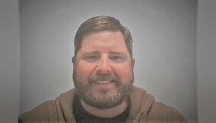 A smiling man with a beard against a blurred background.