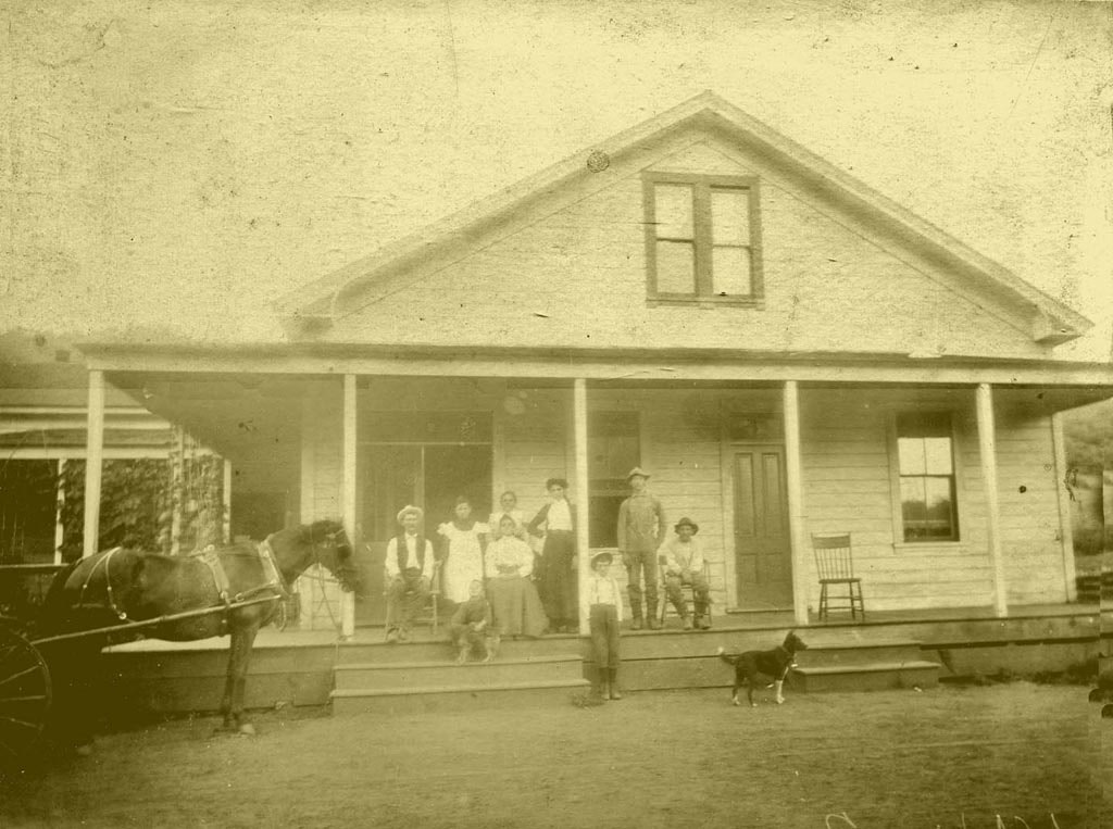 An old photograph of a family outside their home, with a horse-drawn wagon, a dog, and eight people posing together.