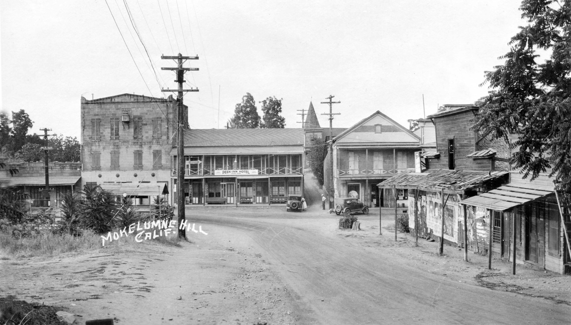 An old black-and-white photo of Mokelumne Hill, California, featuring buildings, a road, and vintage cars from the early 20th century.