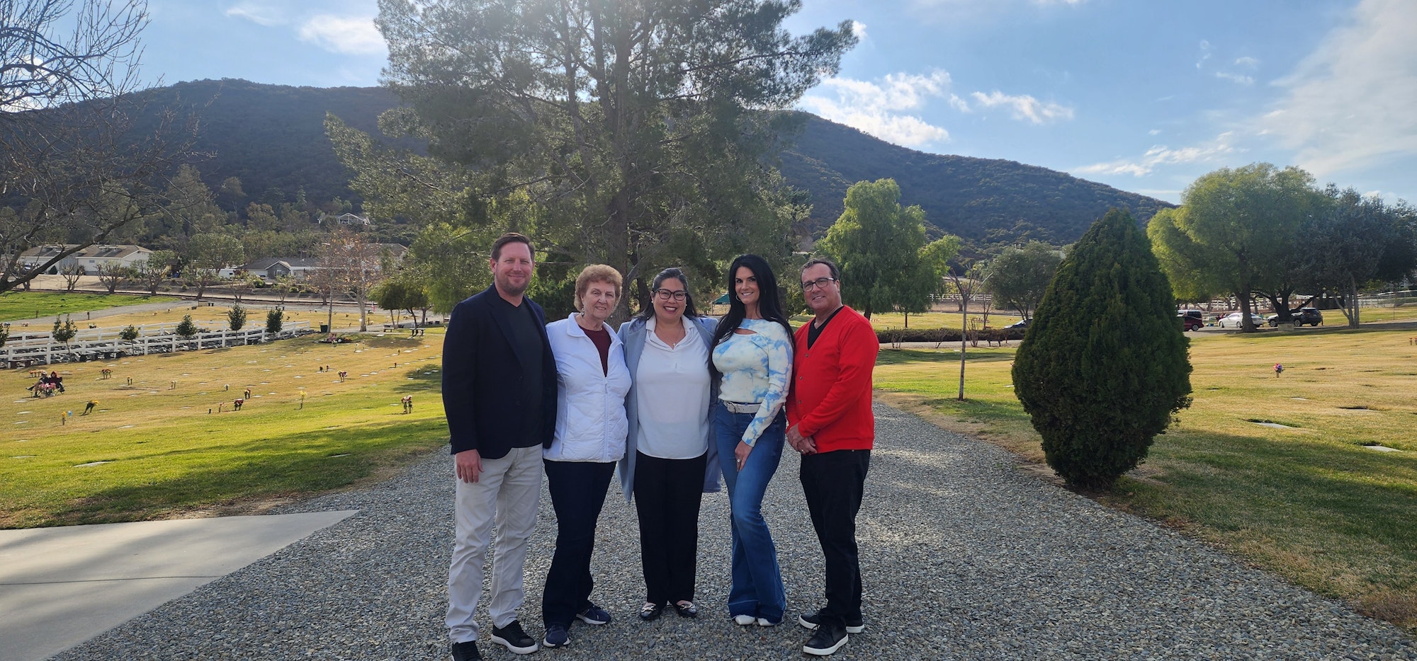 Five people posing outdoors in front of a grassy landscape with hills and trees.