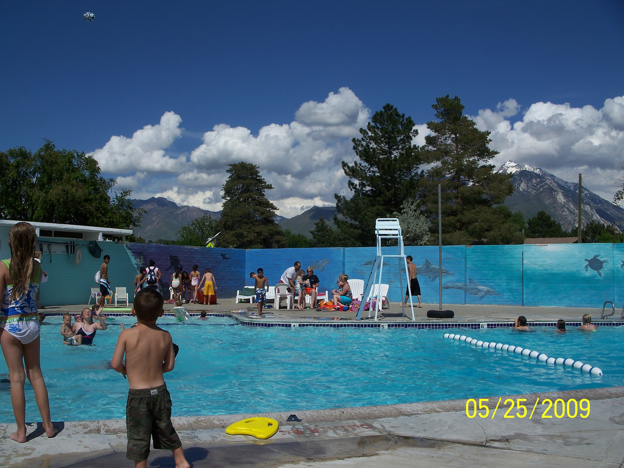 People enjoying a day at the outdoor swimming pool with mountains and clouds in the background.