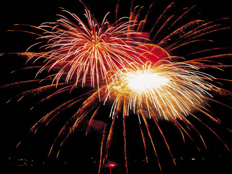 Bright fireworks bursting in the night sky with vivid red and white trails.