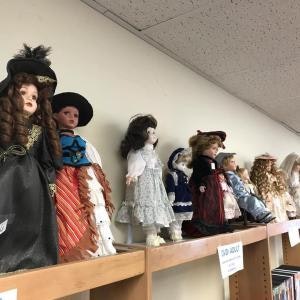 A row of porcelain dolls dressed in vintage attire displayed on a wooden shelf.
