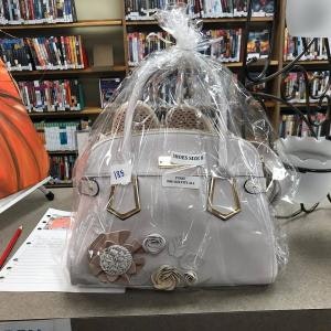 A decorated handbag wrapped in plastic, displayed in a library setting with books and a clipboard nearby.