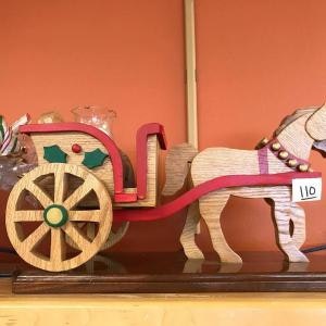 Wooden horse and carriage decoration with a numbered tag, placed on a shelf against an orange background.