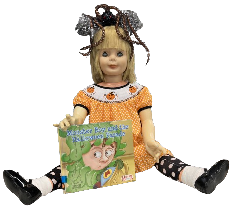 A doll with a Halloween-themed dress and spider hair accessory holds a book titled "Monster Boy and the Halloween Parade."