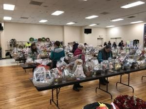 A room with people browsing tables filled with assorted gift baskets wrapped in clear plastic.