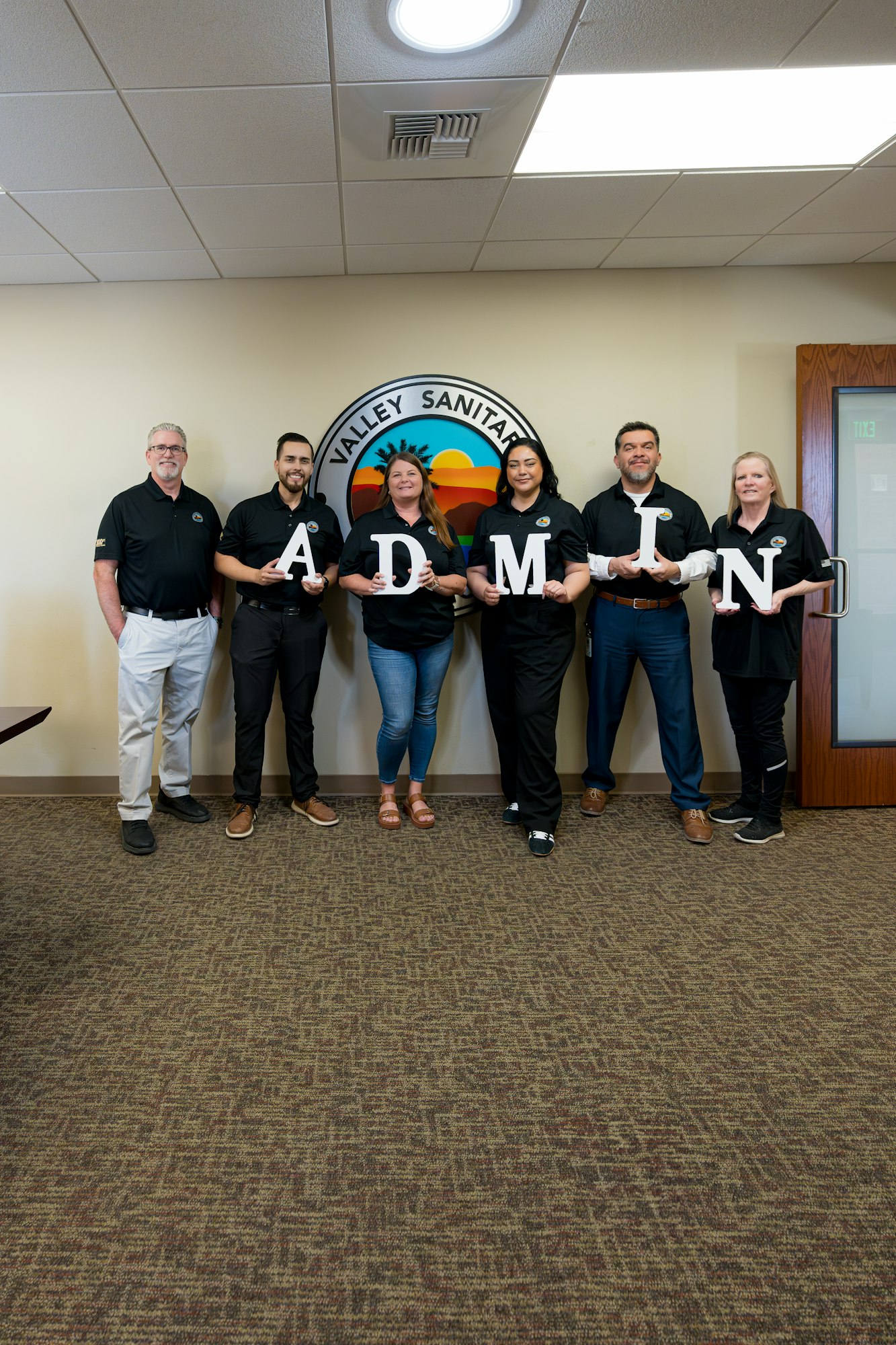 Six people standing, holding letters spelling "ADMIN," in front of a Valley Sanitary seal.