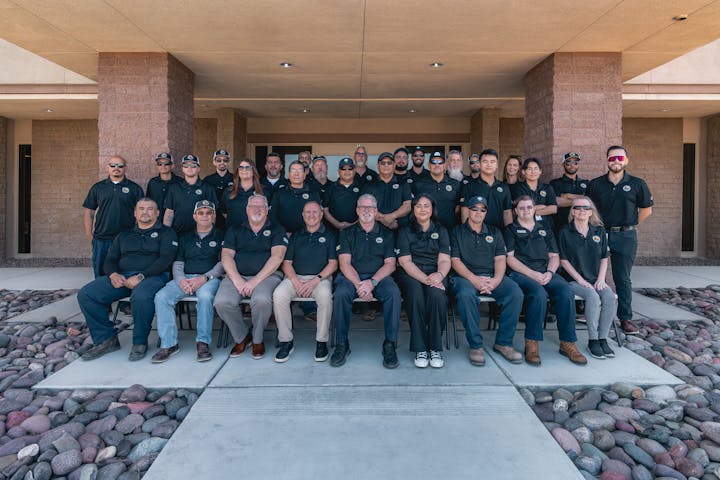 A group of people posing for a photo in matching black shirts, seated and standing outside a building.