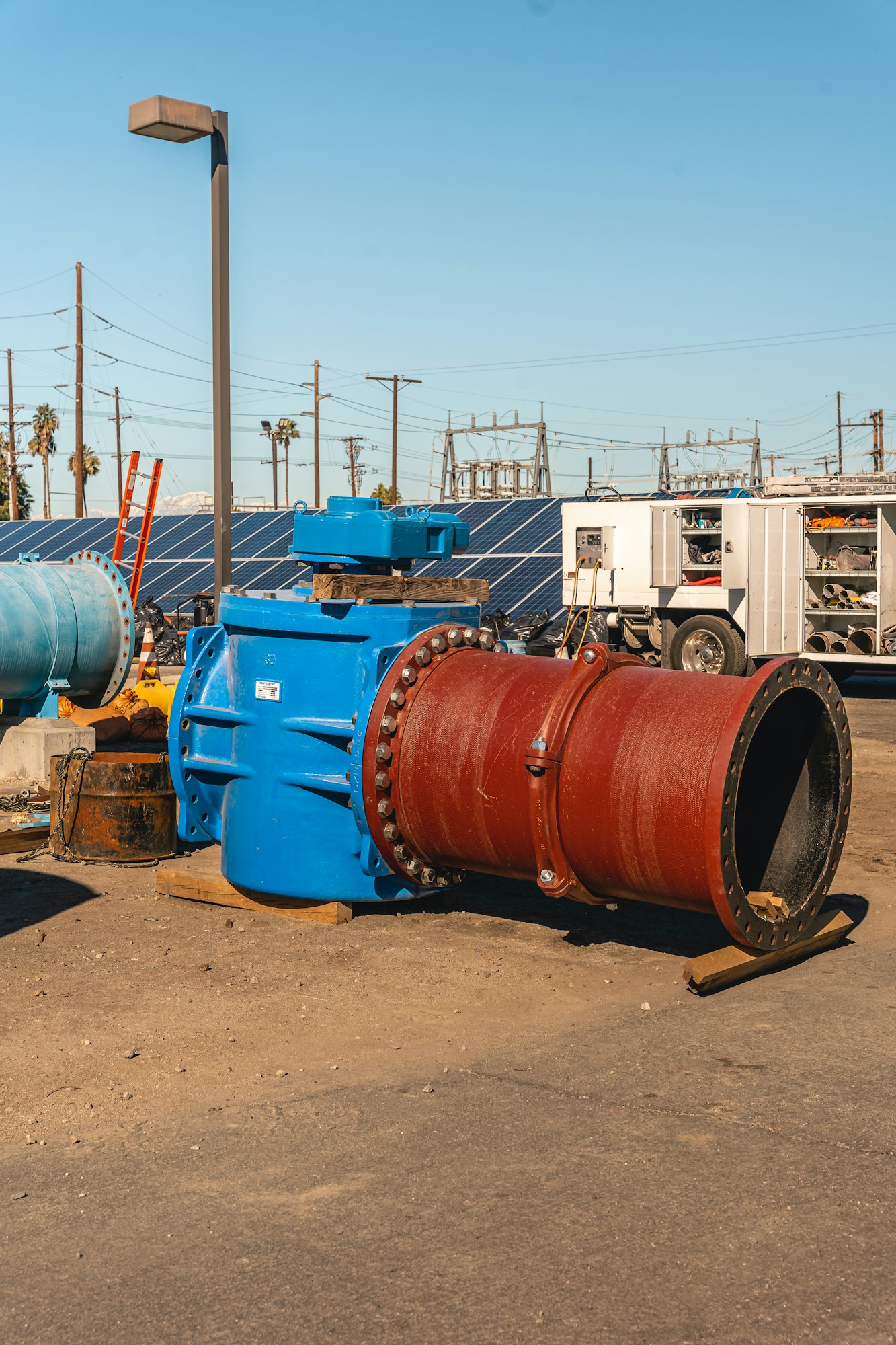 Large industrial pipes, blue and red, near a truck and solar panels at an industrial site.