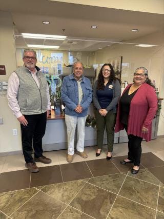 Four people standing together indoors, smiling.