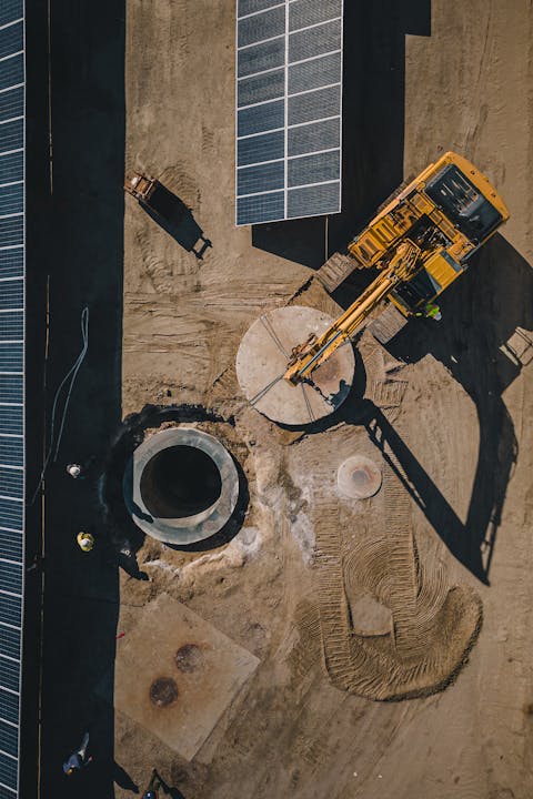 Construction site with solar panels, an excavator, and workers near a large circular structure.