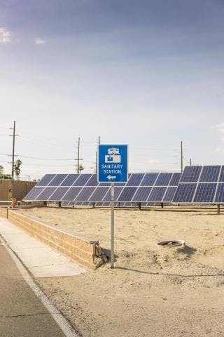 A sign saying "Sanitary Station" stands in front of a field of solar panels in a desert-like area.