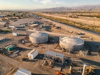 Industrial site with large storage tanks, various structures, and open land under a clear sky.